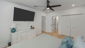 A bedroom with a bed, a TV mounted on the wall, a ceiling fan, and white wardrobes. - With Hot Tub & Mini Golf | Sunny Haven #617 (Fort Walton Beach)