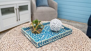 A room with a woven rug, a geometric-patterned tray, a white textured sculpture, a plant in a glass cube, and a white cabinet with glass doors. - With Hot Tub & Mini Golf | Sunny Haven #617 (Fort Walton Beach)