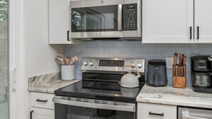 A modern kitchen with white cabinets, stainless steel appliances, a kettle, a coffee maker, and a knife block. - With Hot Tub & Mini Golf | Sunny Haven #617 (Fort Walton Beach)
