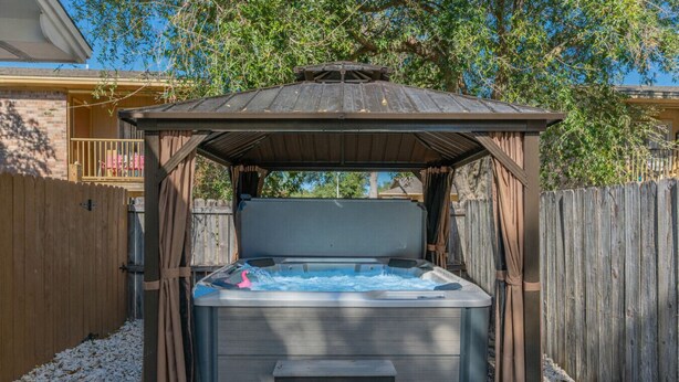 A hot tub with a wooden pergola structure, surrounded by a wooden fence and a gravel area. - With Hot Tub & Mini Golf | Sunny Haven #617 (Fort Walton Beach)