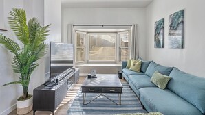 A modern living room with a blue sofa, a coffee table, and a large window with blinds. - 4BD/3BA MTN Views/HTUB Close to Ski Resorts (Cottonwood Heights)