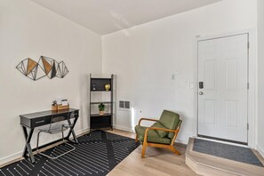Una habitación moderna con un rugido a rayas negras y blancas, un escritorio con silla, un sillón verde, un estante negro y una puerta blanca.