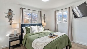 A bedroom with a bed, a nightstand, a lamp, a tray with items, and a TV. - 4BD/3BA MTN Views/HTUB Close to Ski Resorts (Cottonwood Heights)