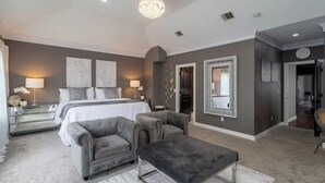 A bedroom with a large bed, two armchairs, a small table, and a mirror on the wall.