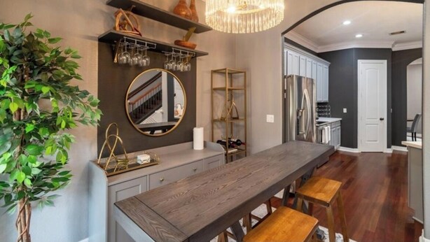 A modern kitchen with a wooden dining table, a chandelier, and a potted plant.