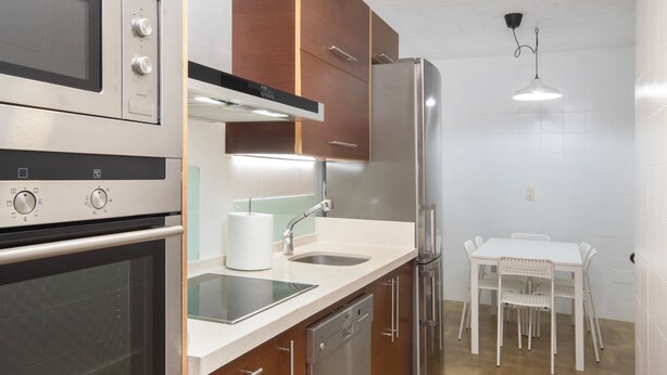 A modern kitchen with stainless steel appliances, a dishwasher, and a dining area with a table and chairs.