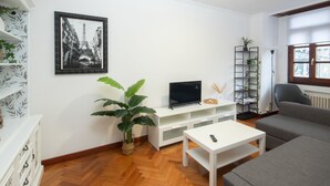 A living room with a white entertainment unit, a large potted plant, a grey sofa, and a framed picture of the Eiffel Tower.