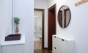 Um corredor estreito com uma pia branca, um espelho e uma porta de madeira que dá para um banheiro.