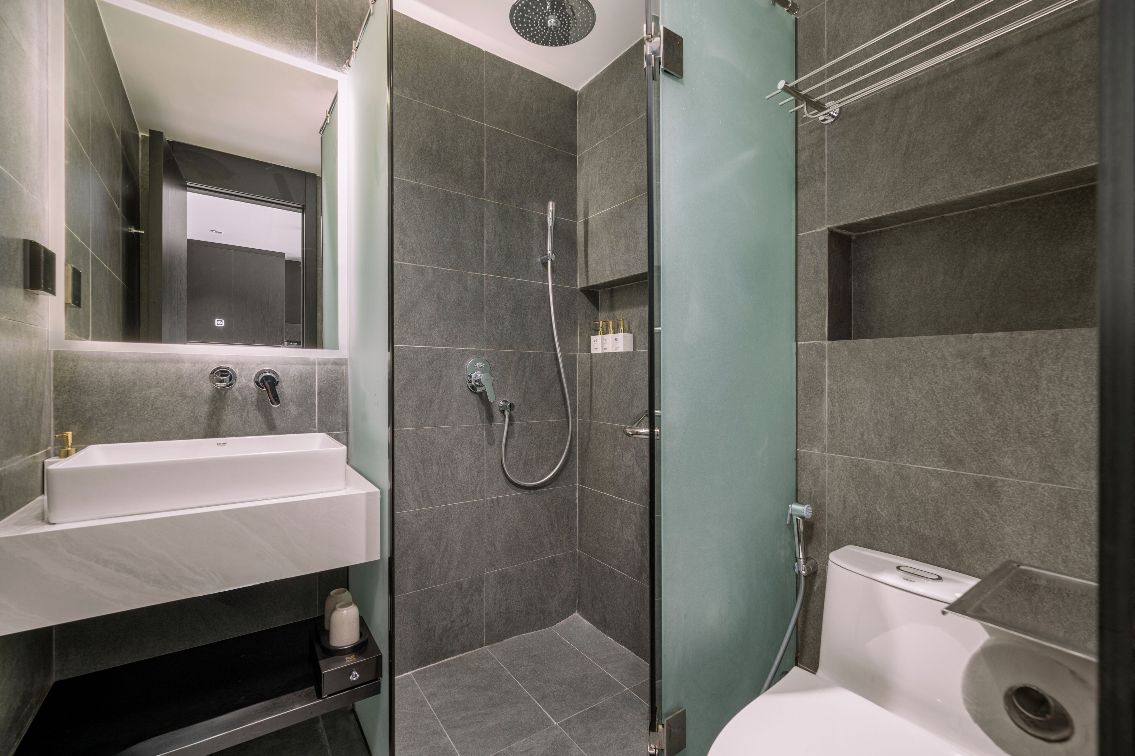 Egy modern fürőszoba üvegfalas zuhanyzóval, fehér mosdókagylóval és WC-vel.