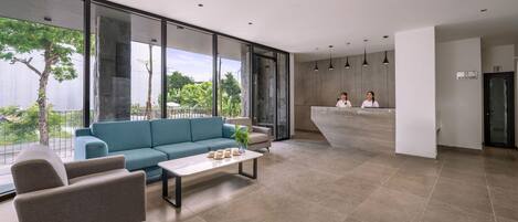 A modern lobby with a reception desk, seating area, and large windows offering a view of greenery.
