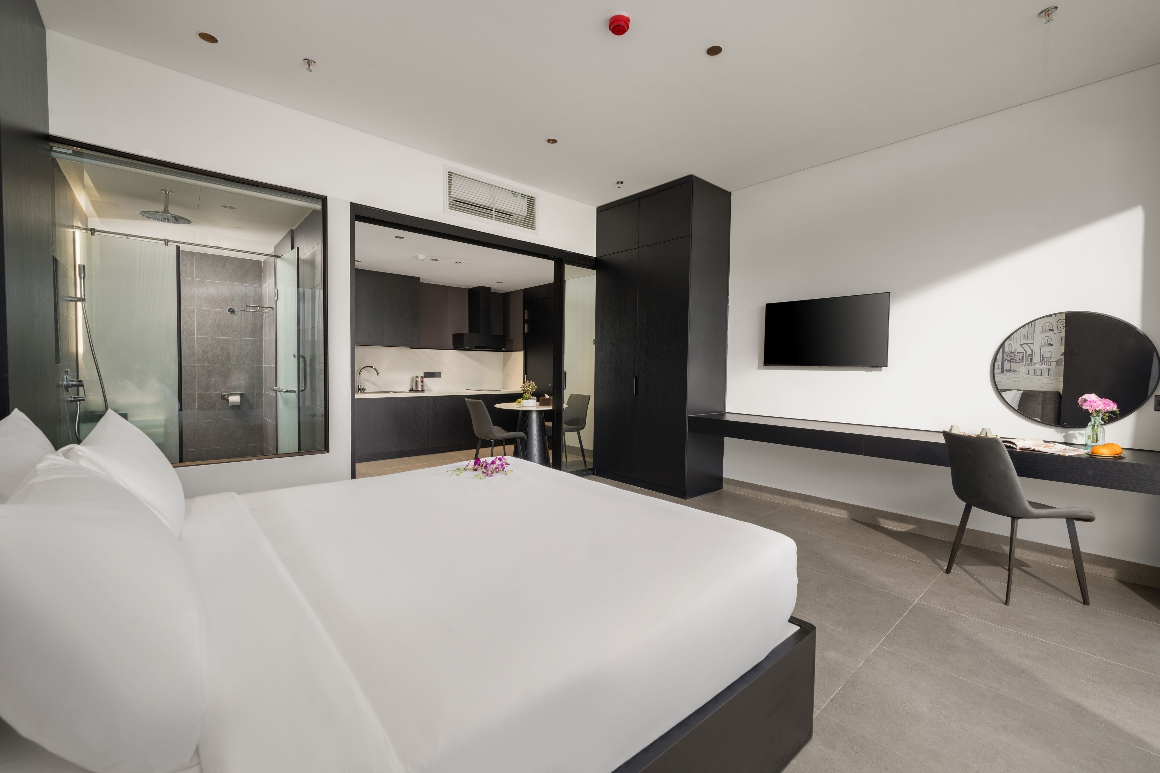 Habitación de hotel moderna con una cama grande, un escritorio, una silla, un televisor y zona de ducha.