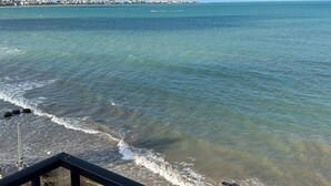A coastal view from a balcony with a clear sky, ocean waves, and distant buildings.