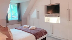 Un dormitorio con cama, televisor montado en la pared y ventana con cortinas.