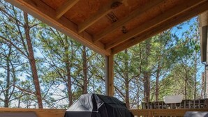 A covered outdoor seating area with chairs and a grill, surrounded by trees. - Large Home in Hoover minutes from the MET! (Birmingham)