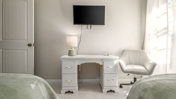 A bedroom with a white dresser, a chair, a bed, and a TV mounted on the wall. - Large Home in Hoover minutes from the MET! (Birmingham)