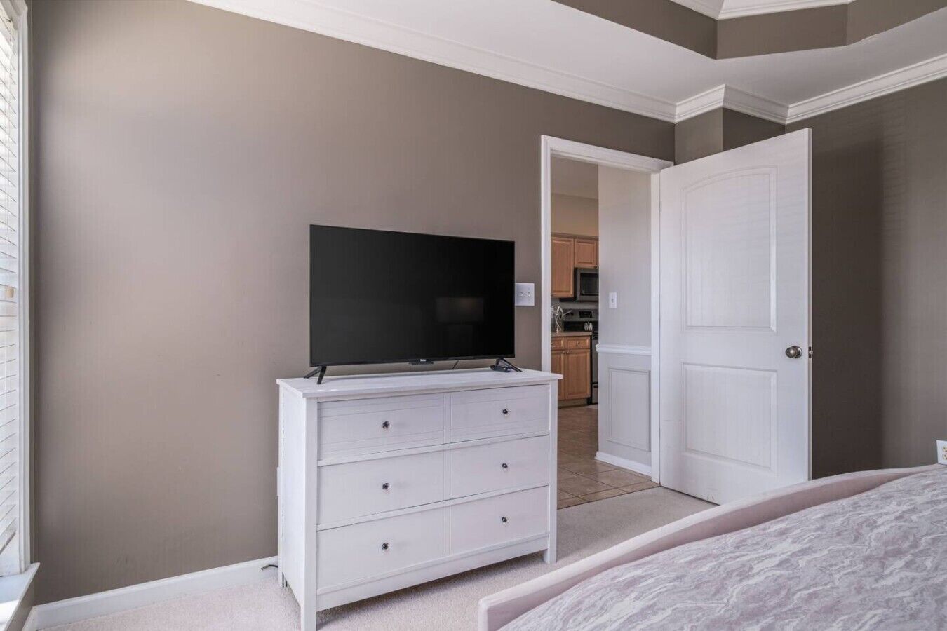 Ein Schlafzimmer mit Fernseher auf einer Kommode, einer Tür zu einer Küche und einem Bett.