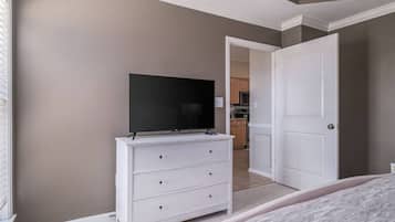 Ein Schlafzimmer mit Fernseher auf einer Kommode, einer Tür zu einer Küche und einem Bett.