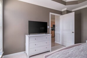 A bedroom with a TV on a dresser, a door to a kitchen, and a bed. - Large Home in Hoover minutes from the MET! (Birmingham)