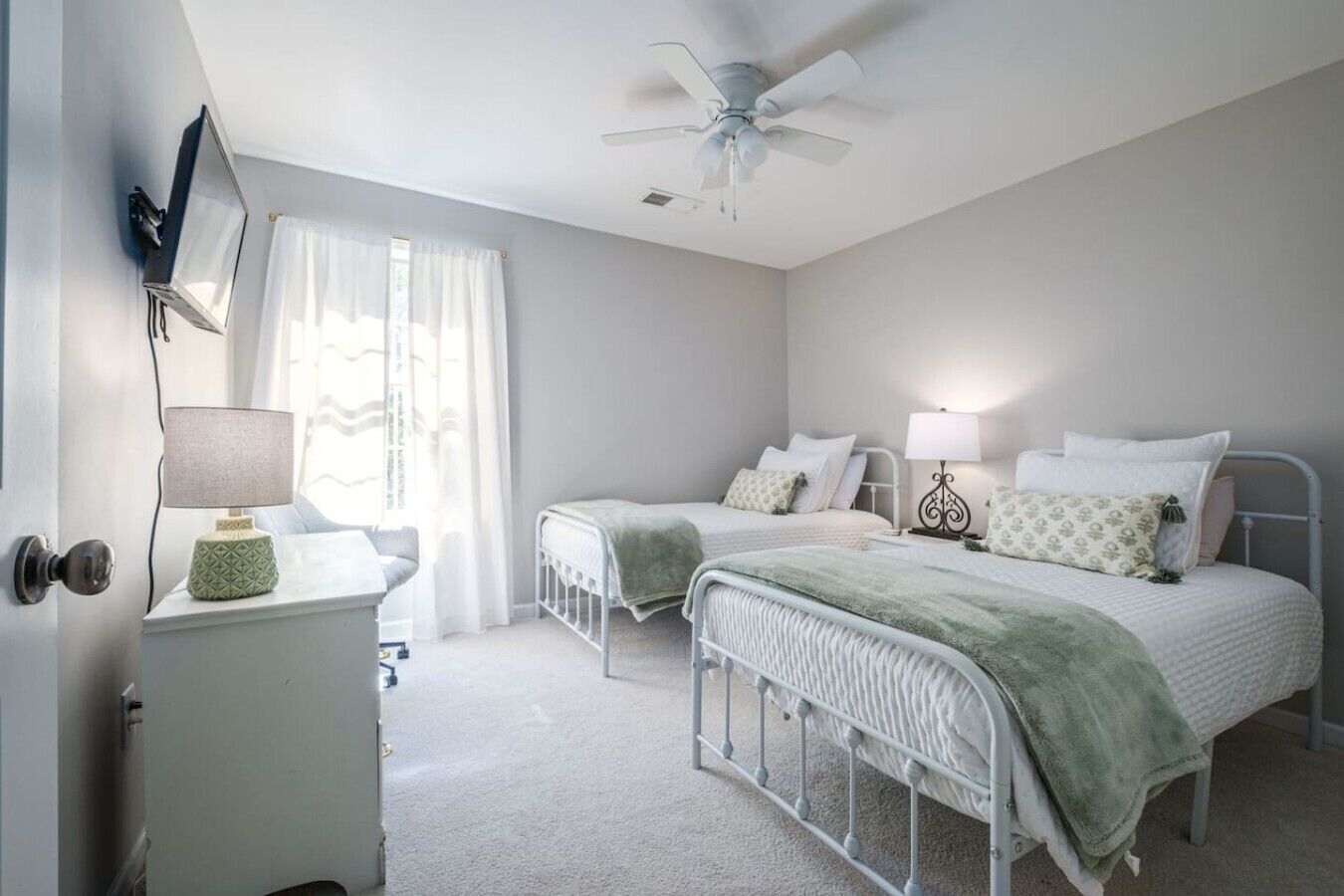 A bedroom with two beds, a ceiling fan, and a desk with a lamp.
