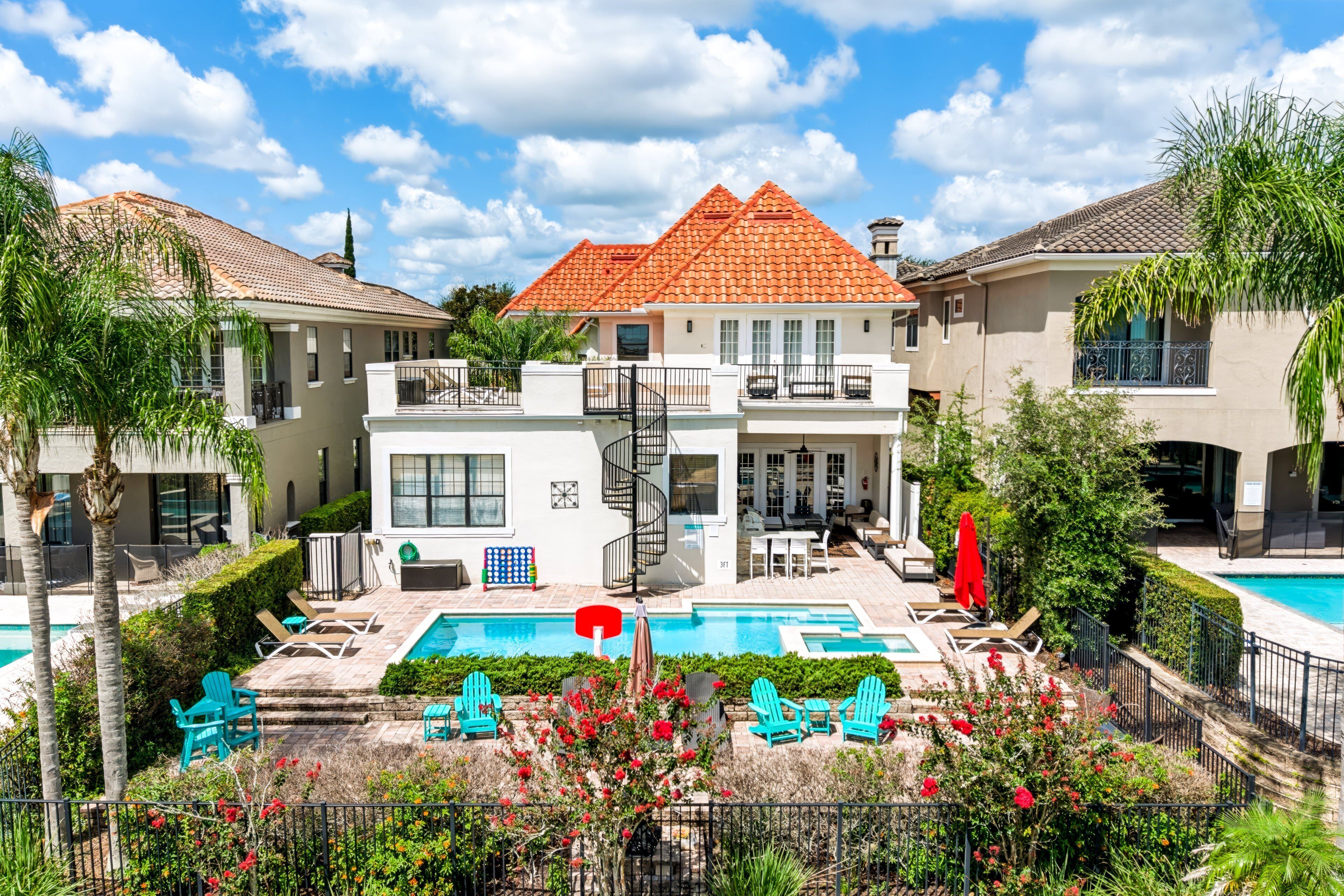 A two-story building with a red-tiled roof, a swimming pool, and outdoor seating.