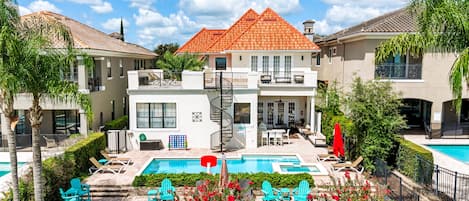 A two-story building with a red-tiled roof, a swimming pool, and outdoor seating.