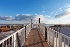 A wooden boardwalk leading to a beach with white railings and a clear sky.