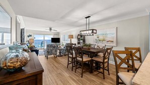 A dining area with a wooden table and chairs, a ceiling fan, and a view of the ocean through large windows. - ☀️ Destin Dream @ Destin Towers | Gulf Front | 12th Floor | Pool | Beachfront 🌊 (Destin)