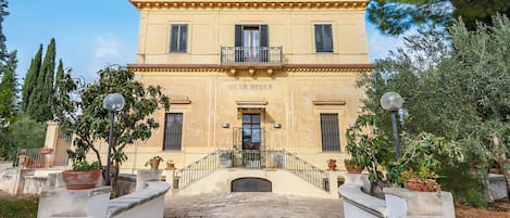 A two-story building with a central entrance, potted plants, and a stone pathway leading to the entrance.