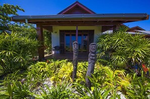 A house with a covered porch, surrounded by tropical plants and two stone statues. - Kula Kai Fiji Oceanfront Villa! Sleeps 15 (Fiji)
