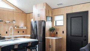 A modern kitchen with wooden cabinetry, a stainless steel refrigerator, a sink with a modern faucet, and bar stools. - Downtown Fruita (Fruita)
