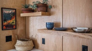 A wooden interior with a shelf holding potted plants, a framed picture, and kitchenware. - Downtown Fruita (Fruita)