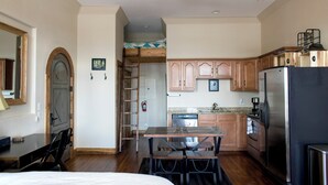 A compact kitchen with wooden cabinets, a stainless steel refrigerator, and a dining area with a table and chairs. - Studio 508 Downtown Leadville (Leadville)