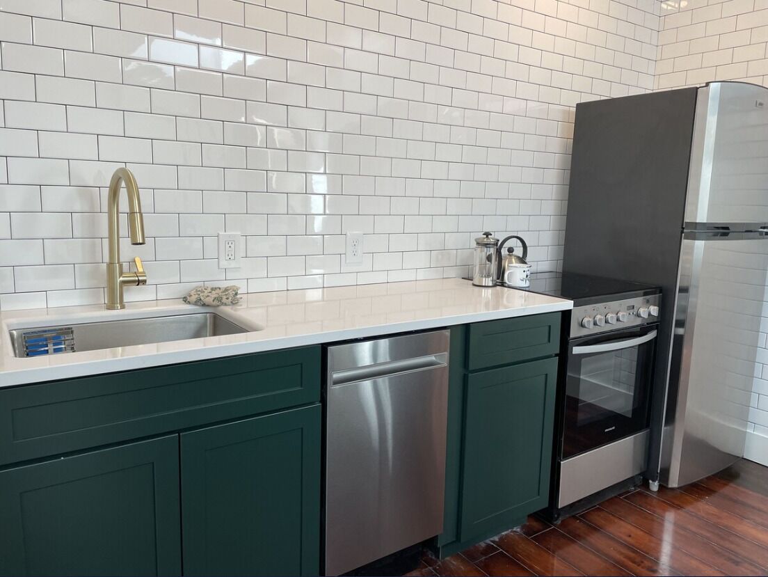 Una cocina con azulejos tipo metro blancos, un lavavajillas de acero inoxidable, un horno empotrado y un refrigerador.
