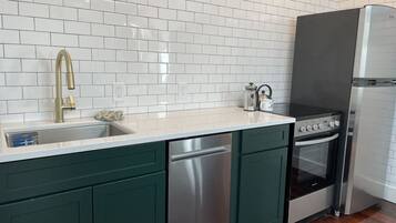 Una cocina con azulejos tipo metro blancos, un lavavajillas de acero inoxidable, un horno empotrado y un refrigerador.