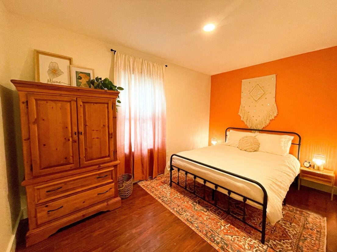 Une chambre avec une armoire en bois, un lit recouvert d’un tapis à motifs et un mur orange.
