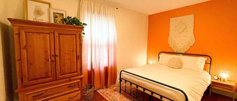 Une chambre avec une armoire en bois, un lit recouvert d’un tapis à motifs et un mur orange.
