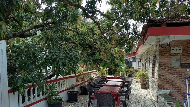An outdoor patio with tiled flooring, multiple tables and chairs, potted plants, and a brick building with a red roof. - Villa AlexMarie guest house  (Candolim)