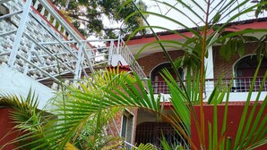 A multi-story building with a red and white facade, a white staircase, and surrounding greenery. - Villa AlexMarie guest house  (Candolim)