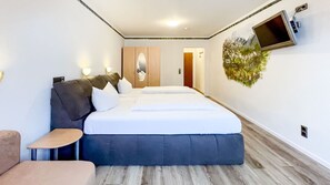 A hotel room with a large bed, a small table, a sofa, a TV mounted on the wall, and a door leading to another room. - A comfortable and versatile room—perfect for relaxation, work, and socializing (Winterberg)