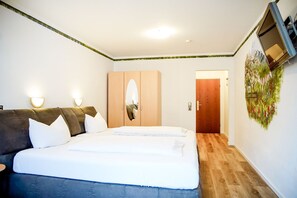 A bedroom with a bed, two bedside tables, a wardrobe, a mirror, a wall-mounted TV, and a door leading to another room. - Comfortable and versatile room -perfect for relaxation, work and exchange (Winterberg)