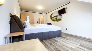 Une chambre d’hôtel moderne, équipée d’un lit, d’une petite table, d’un téléviseur fixé au mur et d’un plancher en bois.