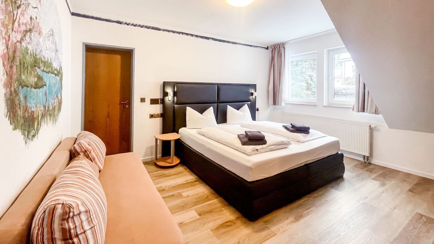 A bedroom with a bed, a bench, a bedside table, a radiator, and a window.