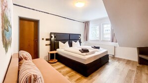 A bedroom with a bed, a bedside table, a window, and a door. - Comfortable and versatile room -perfect for relaxation, work and exchange (Winterberg)