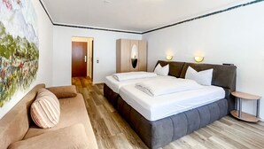 A hotel room with a bed, a sofa, a painting on the wall, and a door. - Comfortable and versatile room -perfect for relaxation, work and exchange (Winterberg)