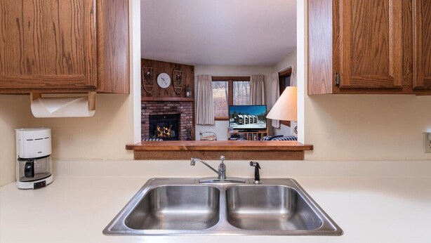 A kitchen with wooden cabinets, a double sink, a coffee maker, and a fireplace. - Kettlebrook Two Bedroom Great Spot for a Skiing Family or Couples (Ludlow)
