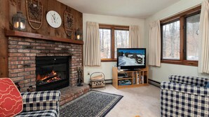 A cozy living room with a brick fireplace, a television, and checkered furniture. - Kettlebrook Two Bedroom Great Spot for a Skiing Family or Couples (Ludlow)