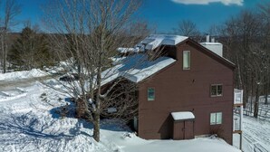 A wooden house with a sloped roof, a small attached shed, and a snow-covered yard. - Kettlebrook Two Bedroom Great Spot for a Skiing Family or Couples (Ludlow)