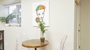 Ein Essbereich mit einem runden Tisch, transparenten Stühlen, einem Blumentopf und einem gerahmten Kunstwerk an der Wand.