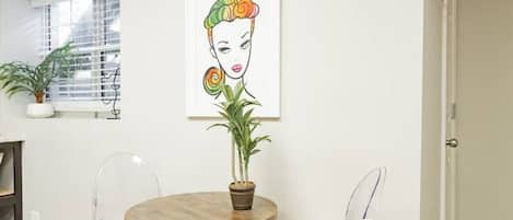 Un coin repas avec une table ronde, des chaises transparentes, une plante en pot et une œuvre d’art encadrée accrochée au mur.