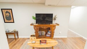 Ein Wohnzimmer mit Fernseher auf einem Holzständer, einem Couchtisch, einem Teppich und einem Bücherregal.